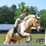 Horse and camper exhibit perfect form as she jumps a beautiful Palomino over a rail.